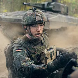 Ein Offizier der Panzertruppe steht im Gelände vor einem Panzer und weist seine Soldaten an