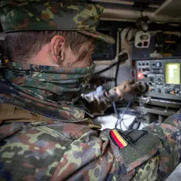 Ein Soldat sitzt in einem gepanzerten Fahrzeug vor einem technischen Gerät
