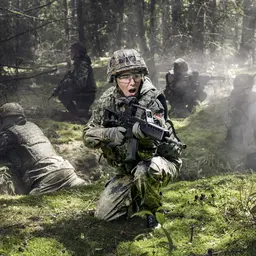 Soldatinnen und Soldaten liegen bei einer Übung auf dem Waldboden und sichern mit Gewehren die Umgebung.