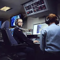 Eine Soldatin der Marine sitzt mit Kopfhörern vor Monitoren.
