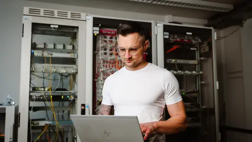Ein Mann steht vor einem Serverschrank und bedient ein Laptop