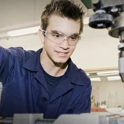 Feinwerkmechaniker mit Schutzbrille arbeitet an einem Bohrständer
