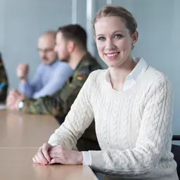Eine Frau sitzt an einem Tisch mit zivilen uns militärischen Mitarbeitern