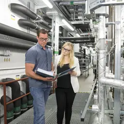 Eine Zivilistin und ein Zivilist schlagen etwas in ihren Unterlagen nach. 