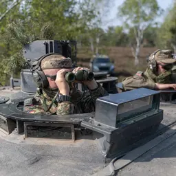 Soldaten mit Fernglas und Maschinengewehr schauen aus der Luke eines Panzers.