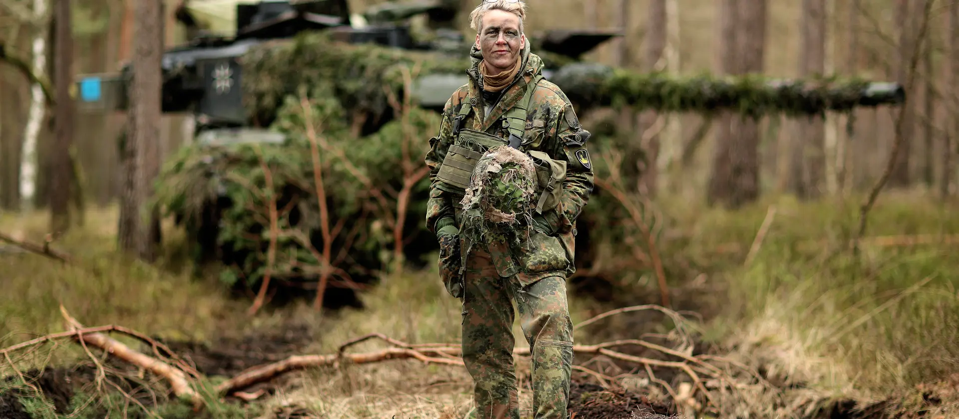 Eine Soldatin steht in einem Wald vor einem Panzer