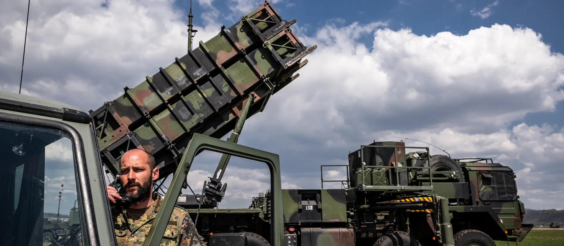 Ein Soldat der Bundeswehr steht an einem Fahrzeug. Im Hintergrund befindet sich ein Raketenabwehrsystem