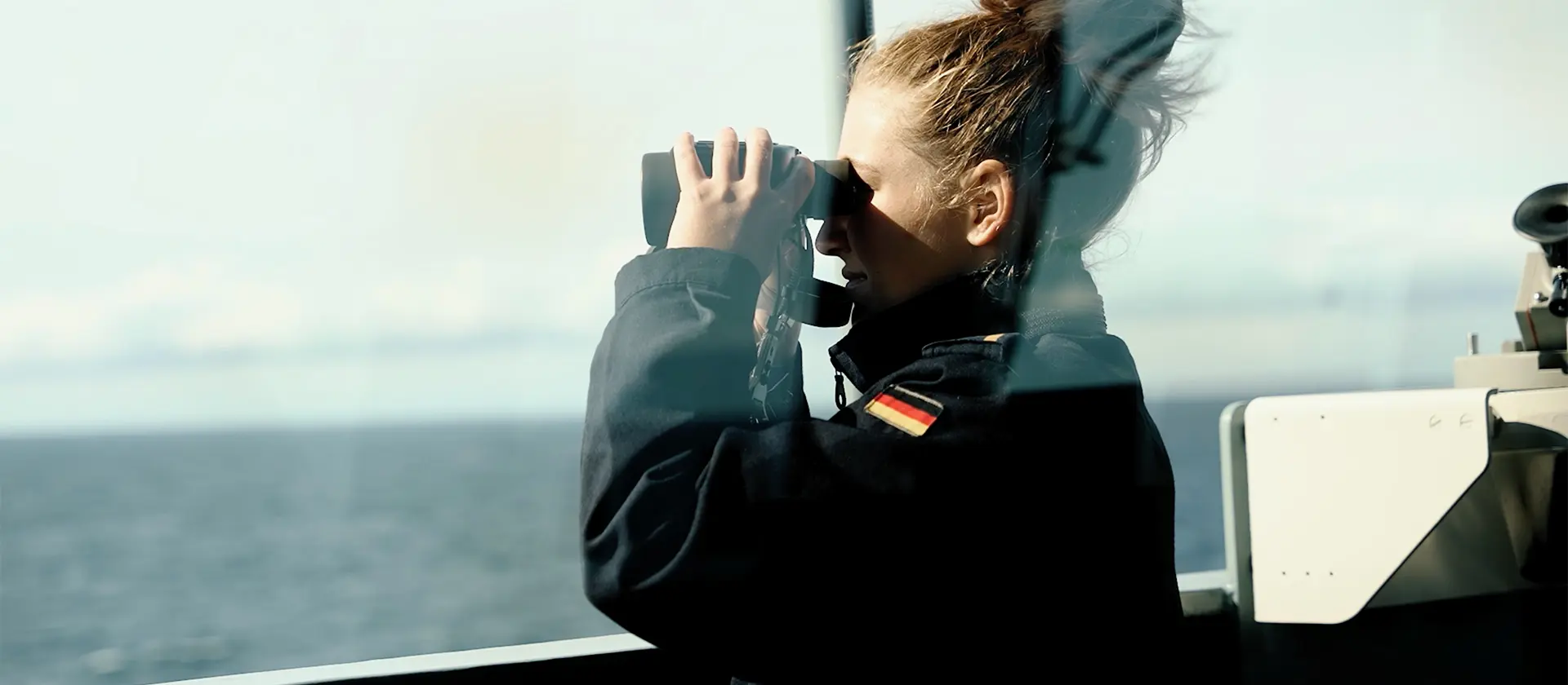 Eine Marinesoldatin schaut durch ein Fernglas aufs Meer hinaus.