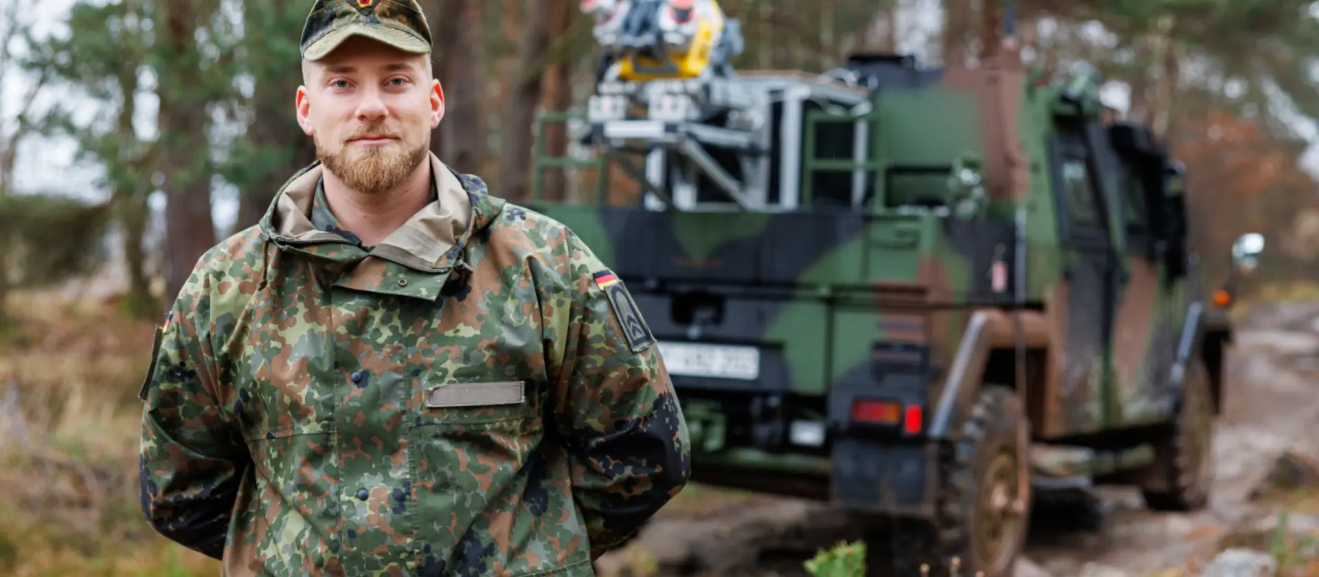 Ein Soldat der Bundeswehr steht im Wald vor einem Fahrzeug