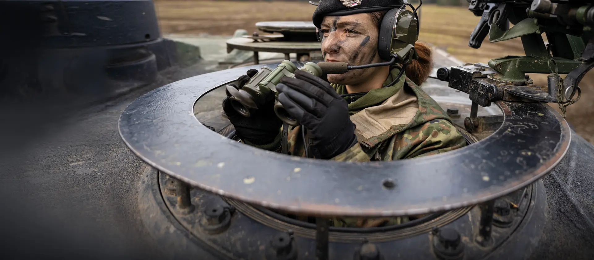 Eine Soldatin schaut mit einem Fernglas in der Hand aus einem Panzer