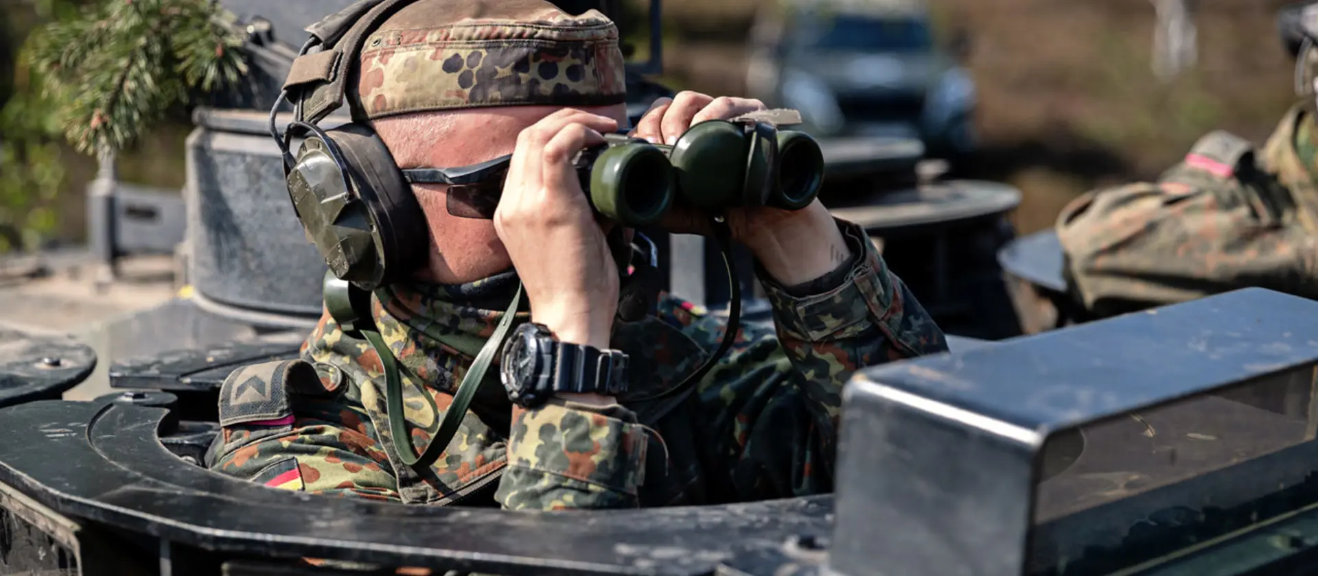 Ein Soldat der Bundeswehr schaut mit einem Fernglas aus einem Panzer