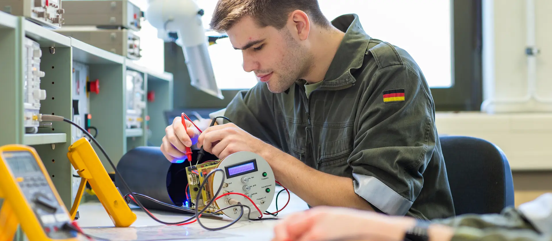 Mann misst mit einem elektronischen Messinstrument die Verkabelung eines technischen Gerätes