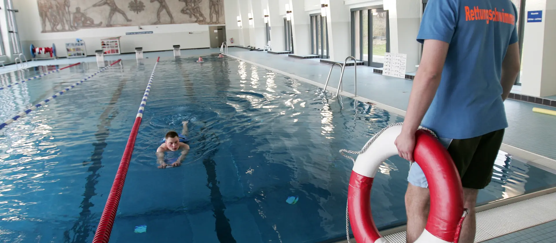 Ein Mann steht mit Rettungsring in der Hand am Rand eines Schwimmbecken