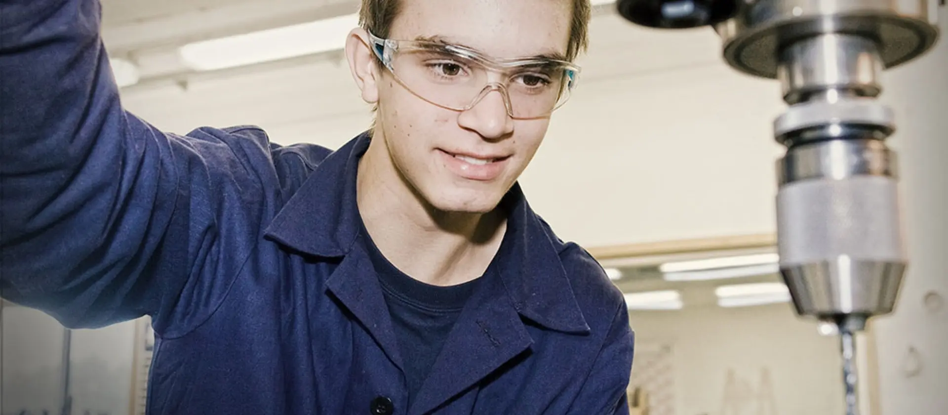 Feinwerkmechaniker mit Schutzbrille arbeitet an einem Bohrständer