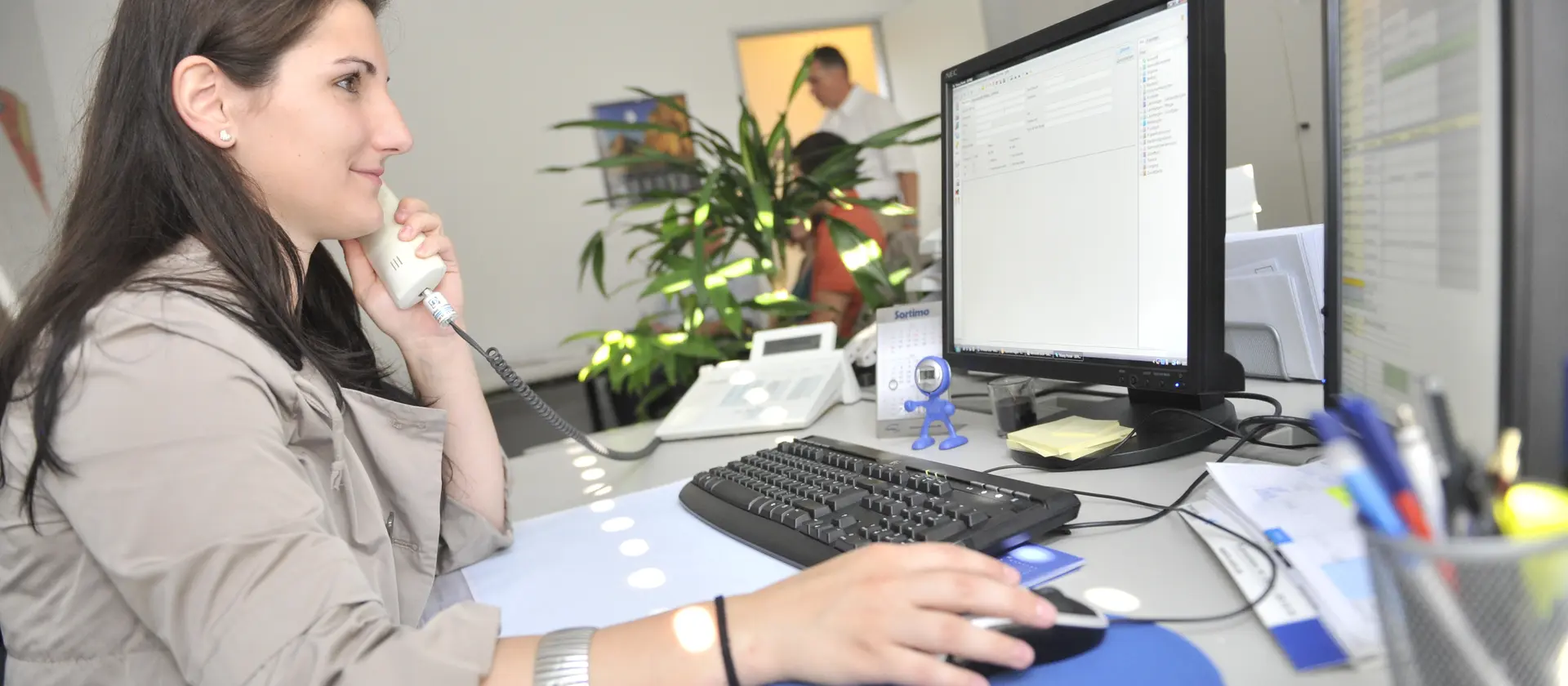 Frau mit langen dunklen Haaren sitzt am Computer und telefoniert