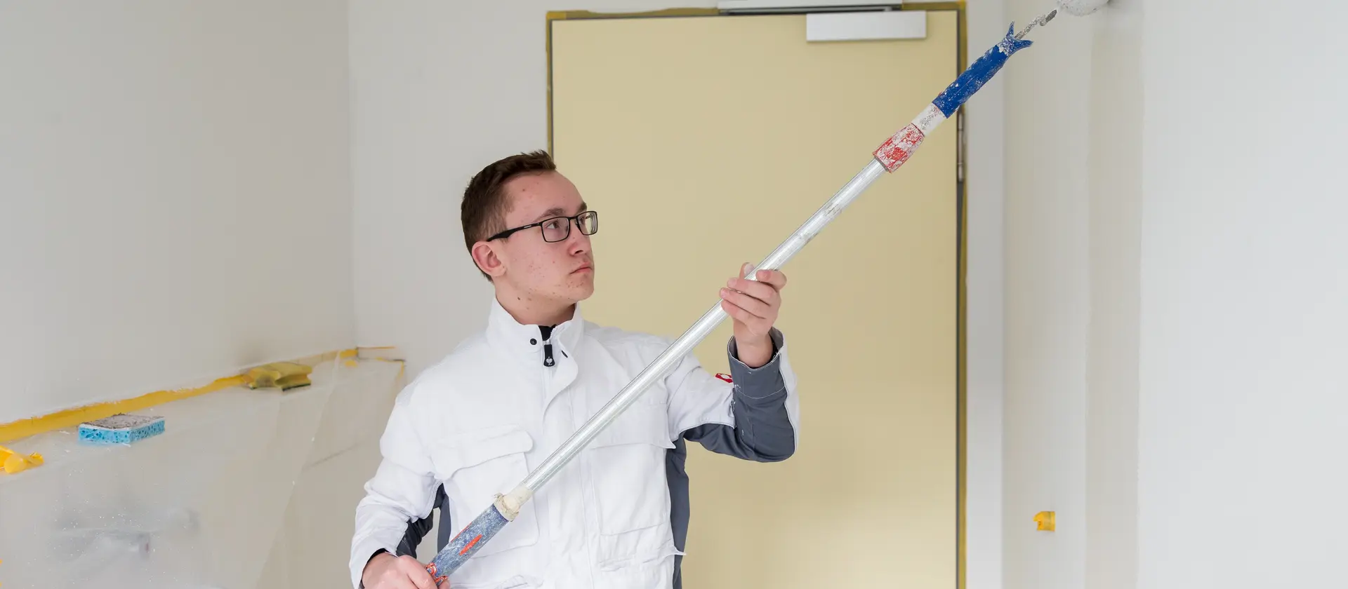 Ein Maler mit Rollenverlängerung streicht eine Wand 