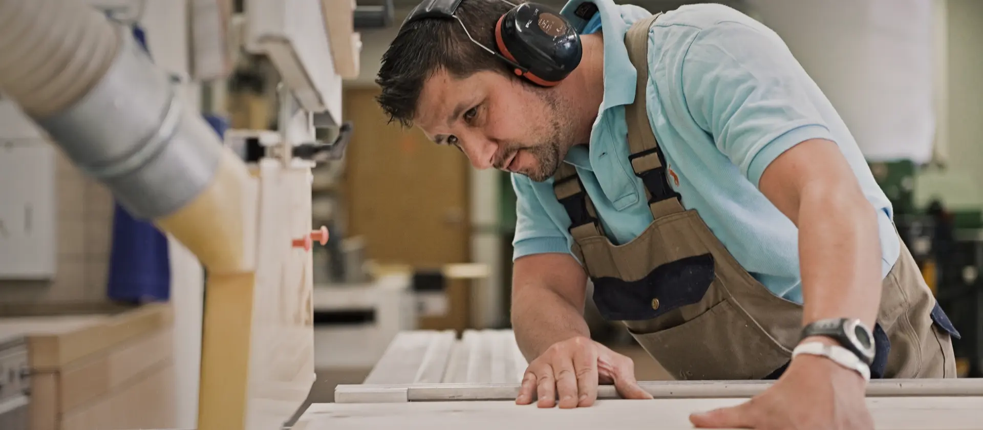 Ein Tischler in Arbeitshose und mit Gehörschutz sägt Holz zu