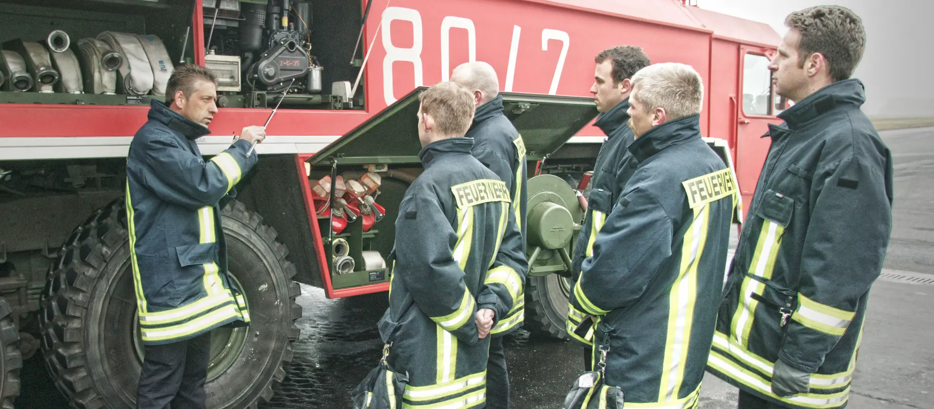 Eine Gruppe Feuerwehrleute steht vor einem Löschfahrzeug und wird geschult