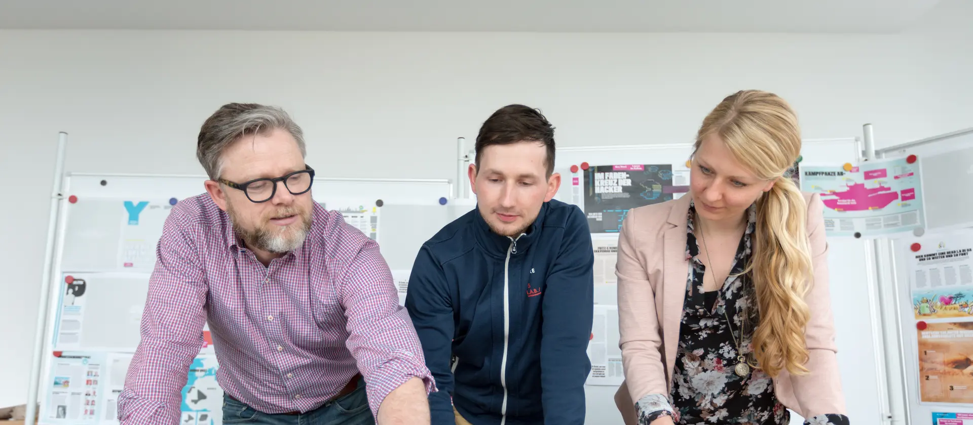 Zwei Herren und eine Dame schauen sich gemeinsam Ausdrucke im Büro an