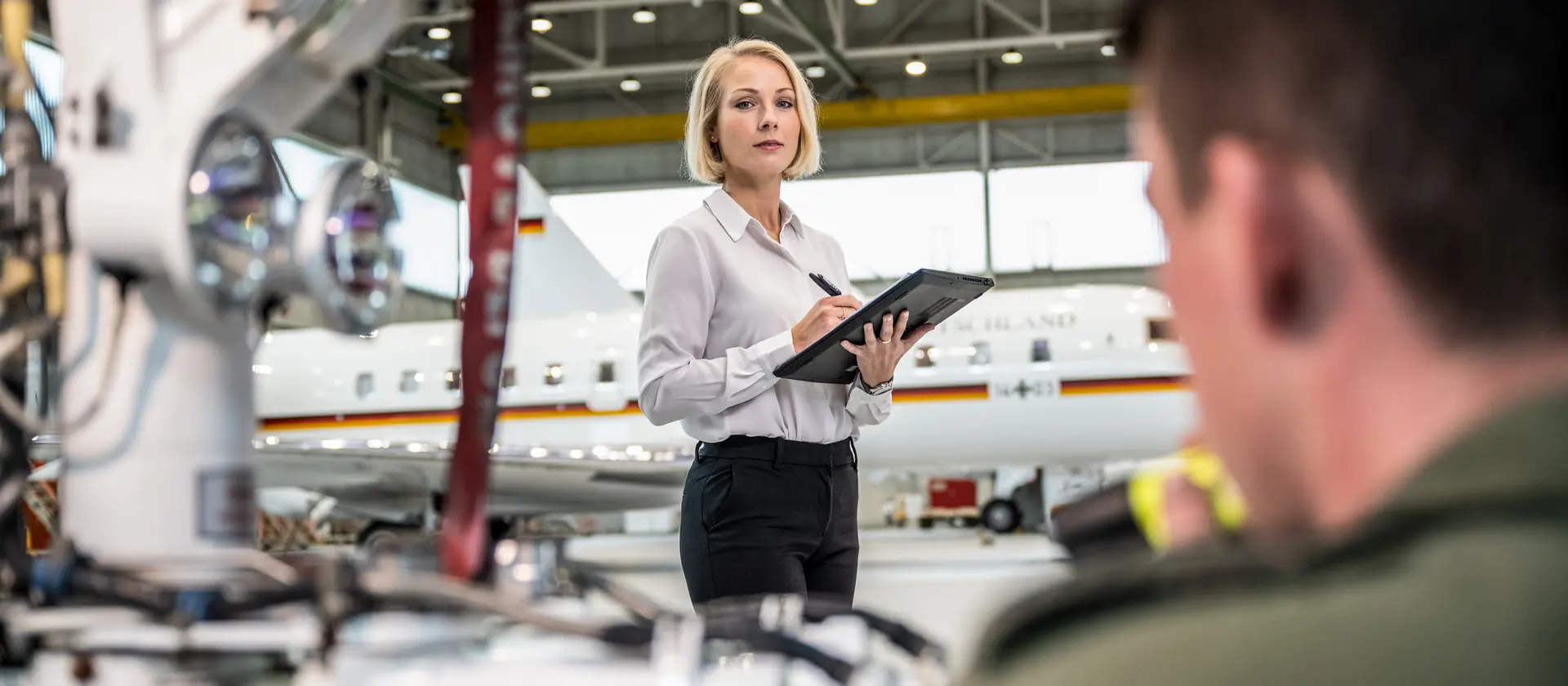 Eine Ingenieurin steht mit einer Kladde vor einem Flugzeug