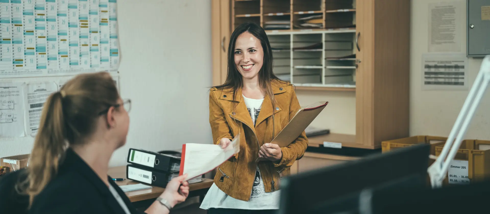 Zwei Frauen arbeiten in einem Büro und tauschen Akten aus