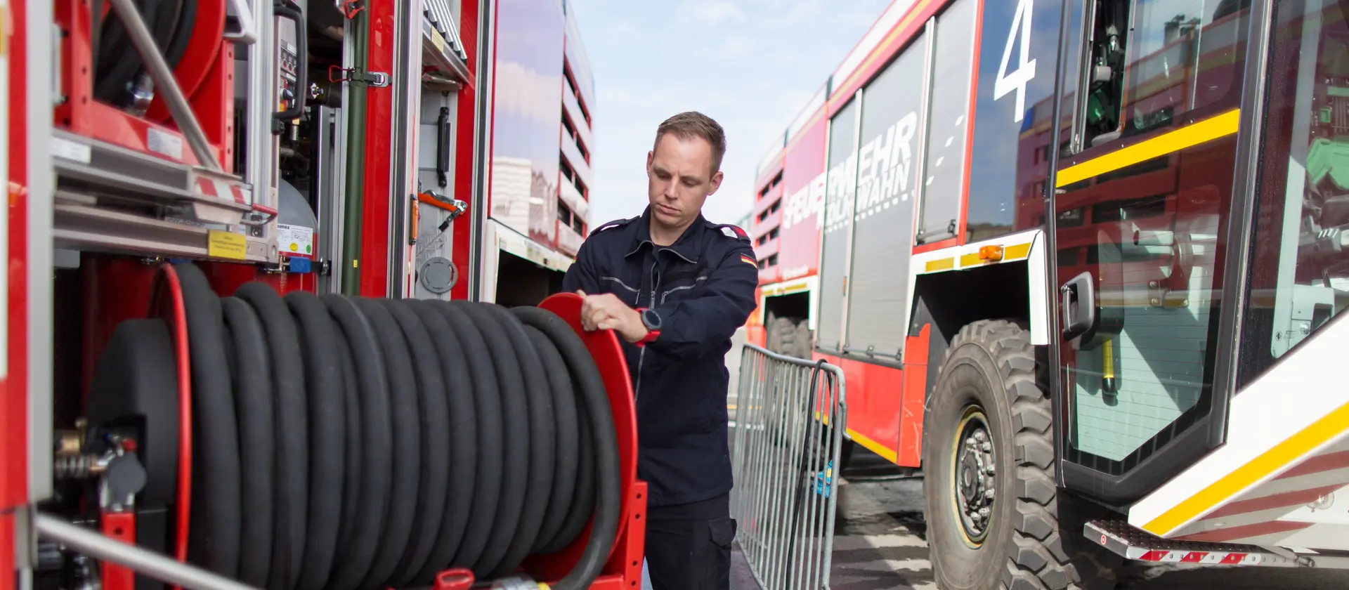 Feuerwehrmann steht an einem Löschfahrzeug und rollt einen Schlauch ein