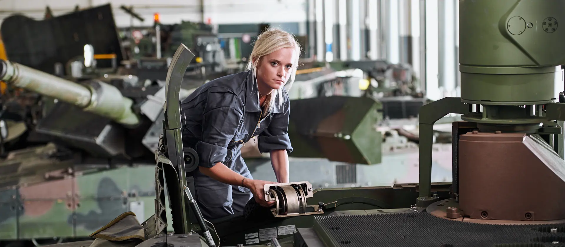 Eine Frau in grauem Arbeitskombi arbeitet an einem militärischen Fahrzeug