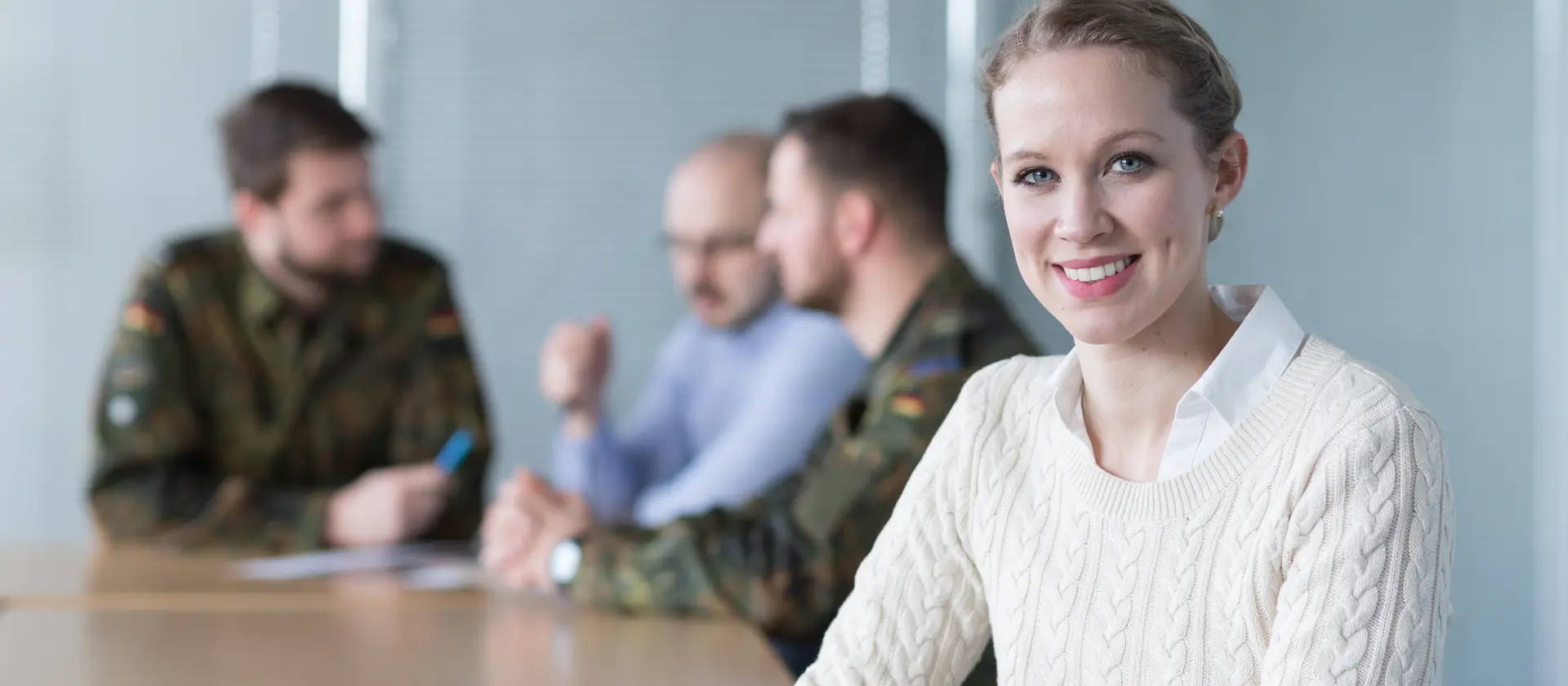 Eine Frau sitzt an einem Tisch mit zivilen uns militärischen Mitarbeitern