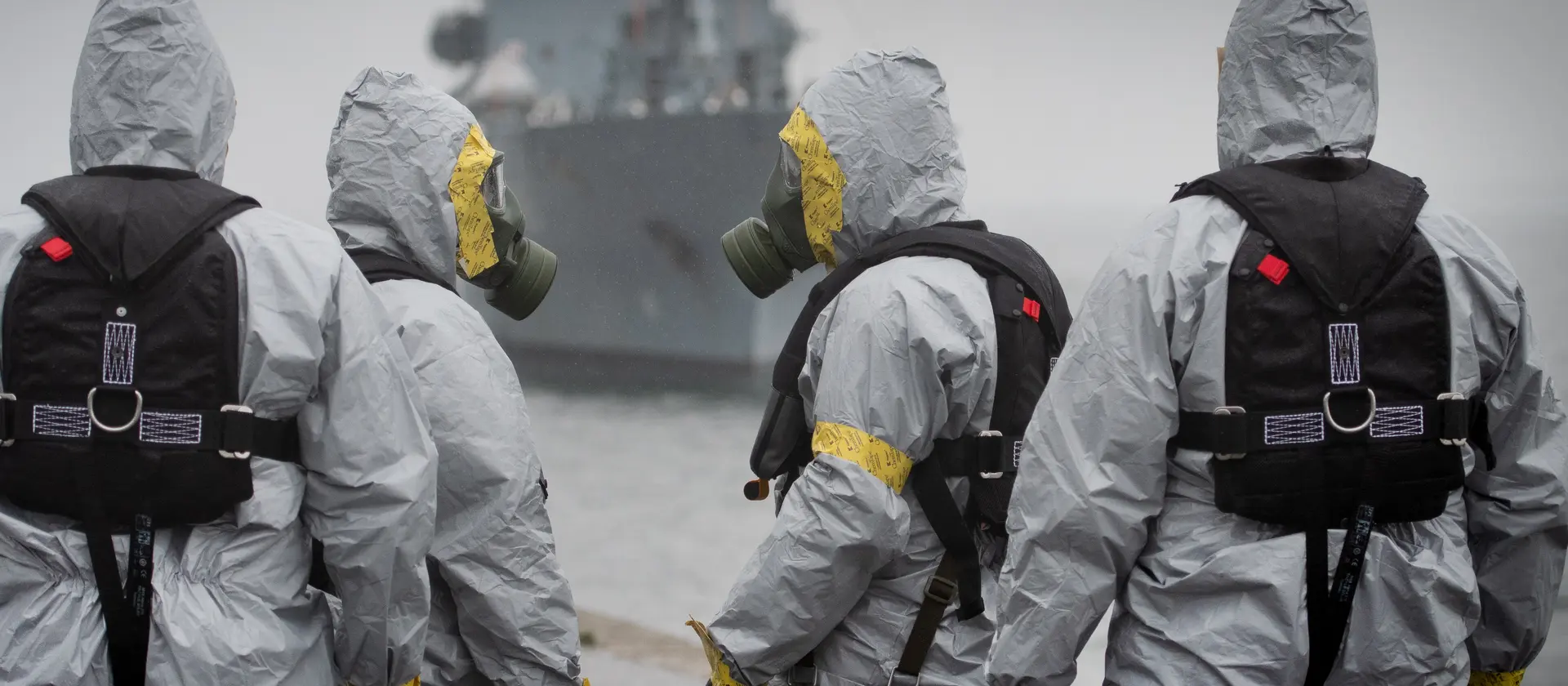Soldaten der ABC Abwehrtruppe stehen in Schutzkleidung vor einem Schiff