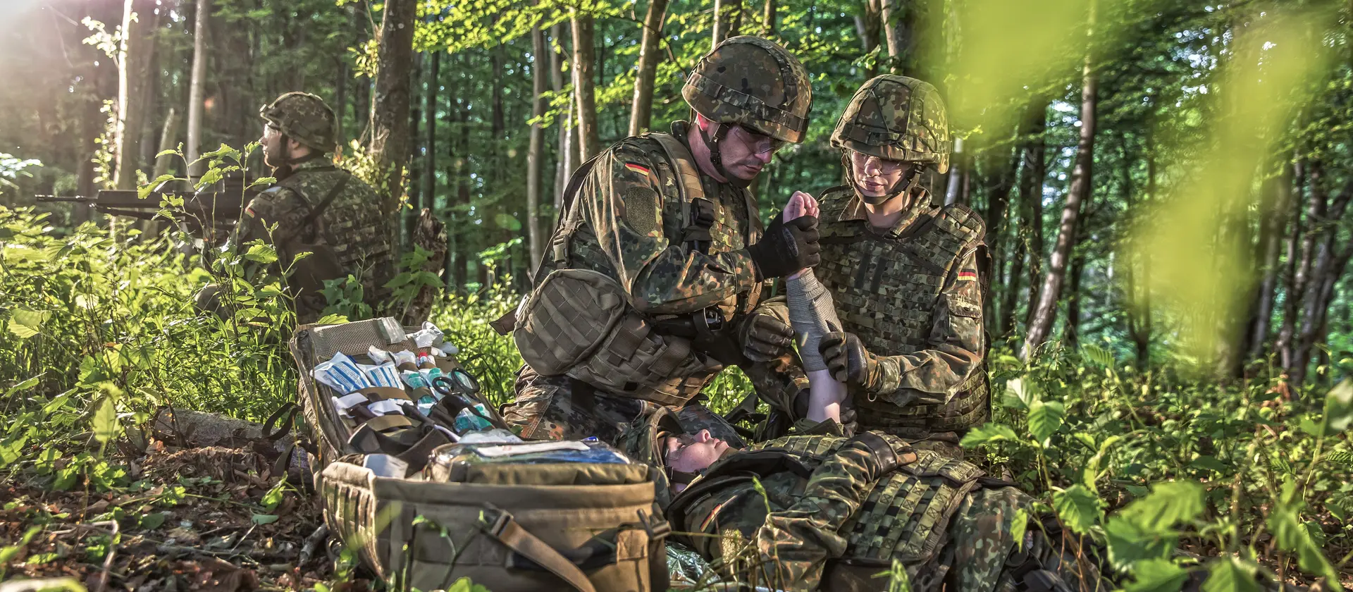 Soldaten im Wald bei einem medizinischen Einsatz. Sie versorgen einen Verwundeten.
