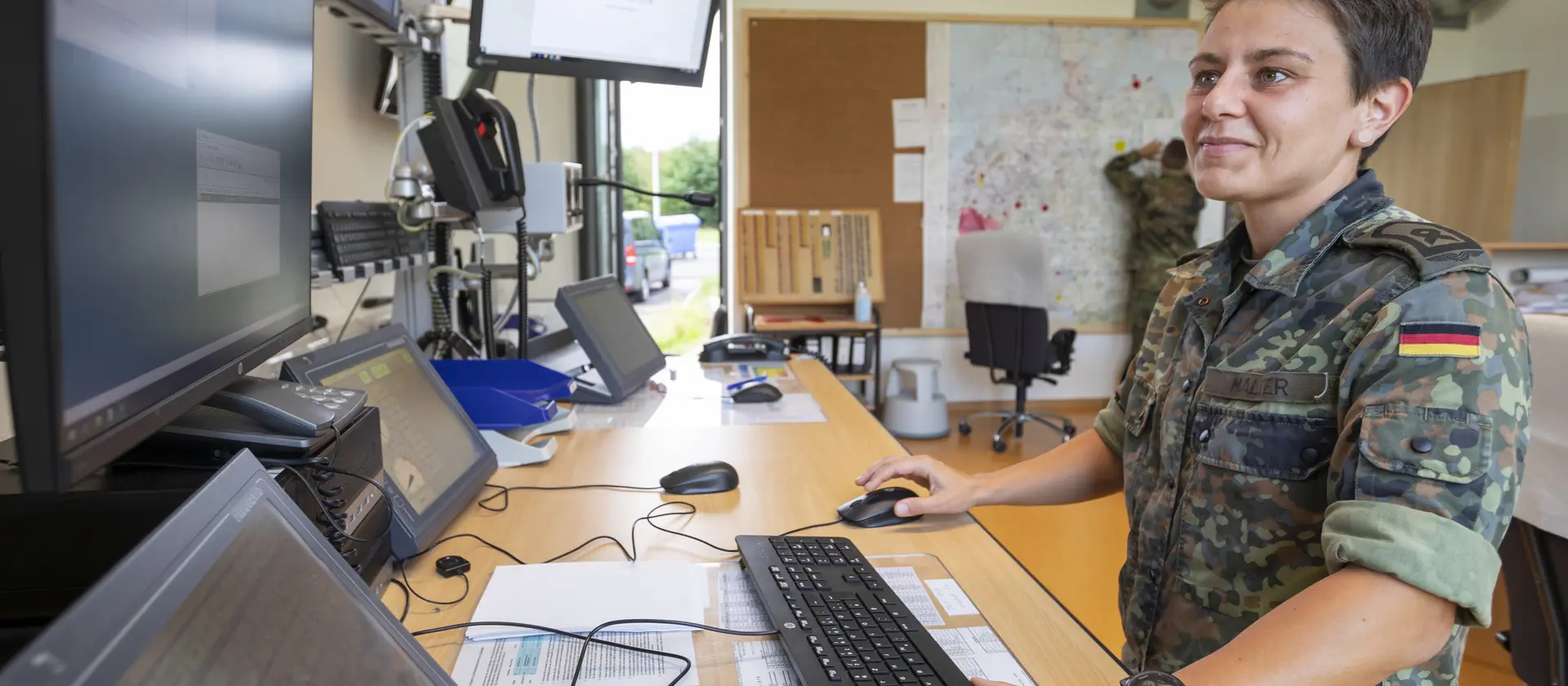 Eine Soldatin steht an ihrem Arbeitsplatz mit vielen Monitoren