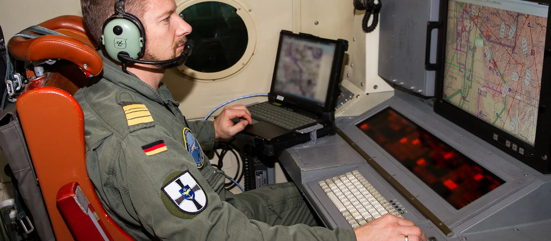 Soldat mit Headset sitzt in einem Flugzeug vor einem Monitor