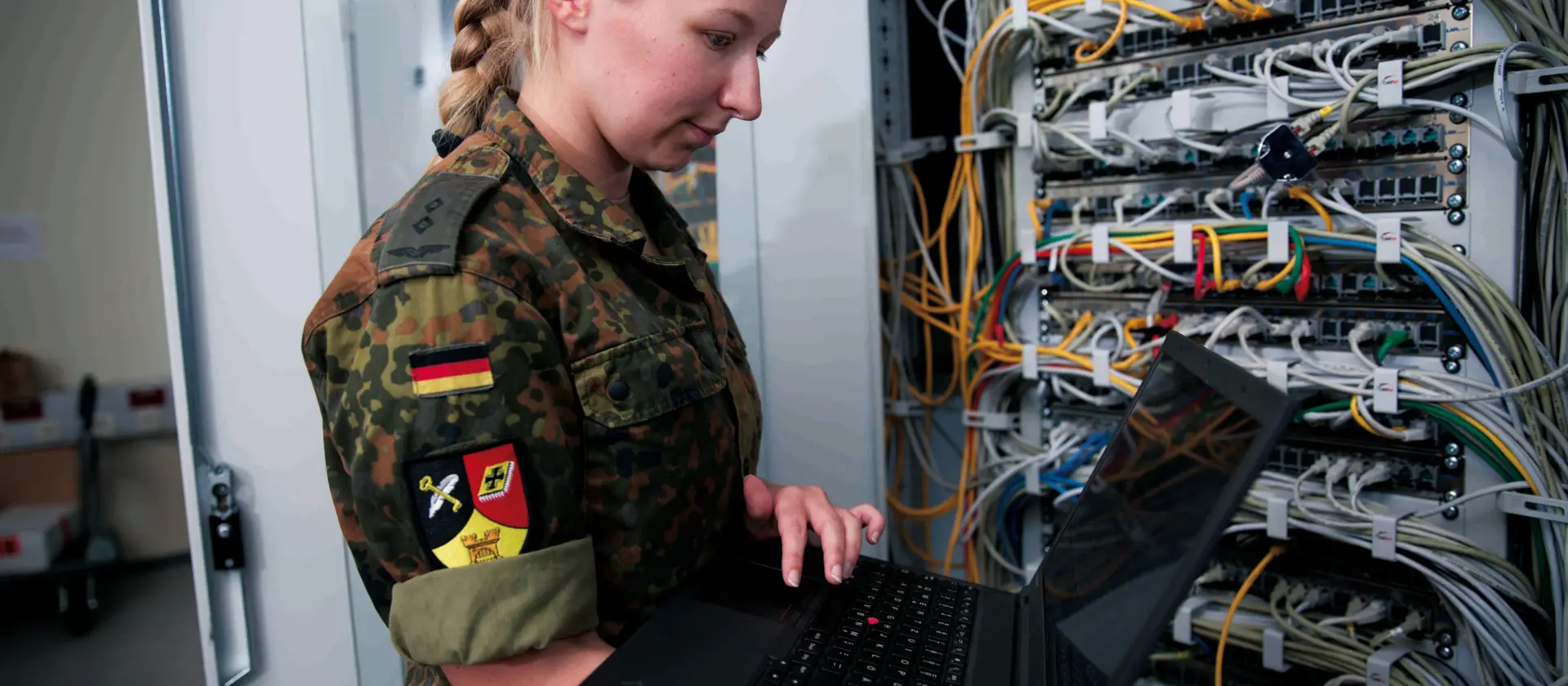 Soldatin mit Laptop prüft Verbindungen eines Servers