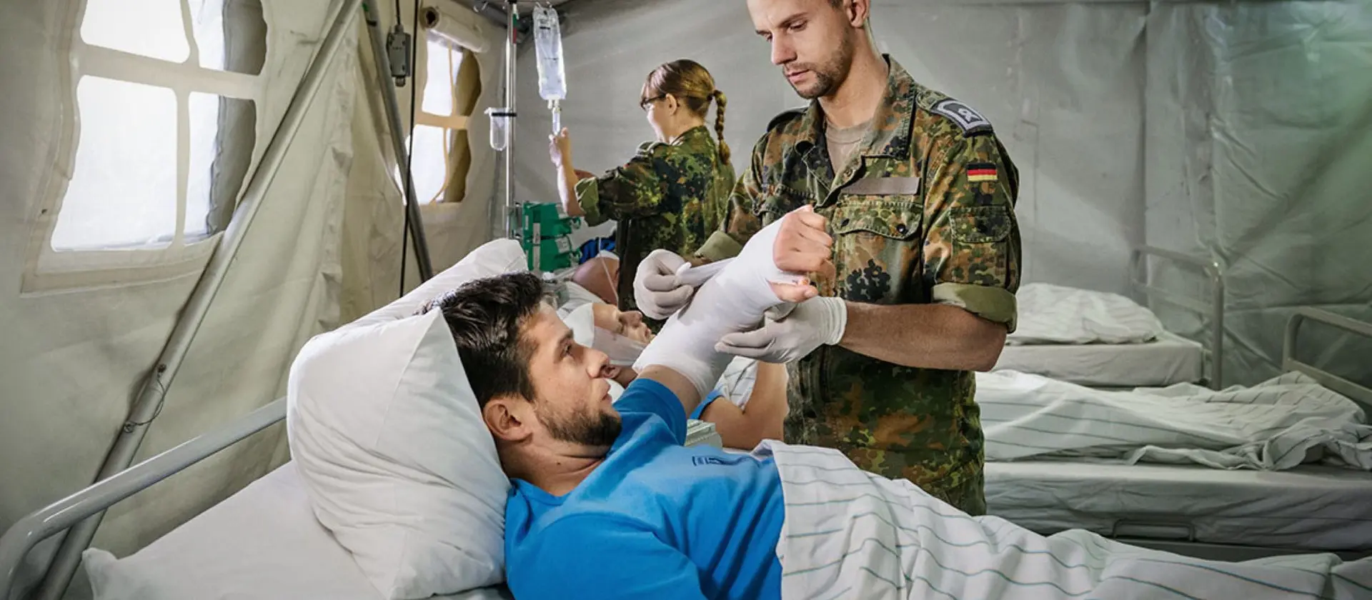 Ein Sanitätsunteroffizier und Pflegefachmann verbindet einem Verwundeten den linken Arm
