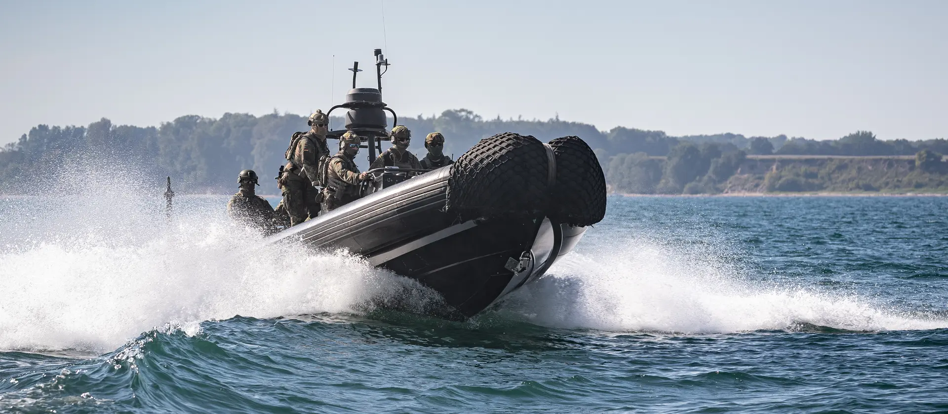 Ein schwarzes Motorboot der Marine fährt mit Soldaten schnell über das Wasser