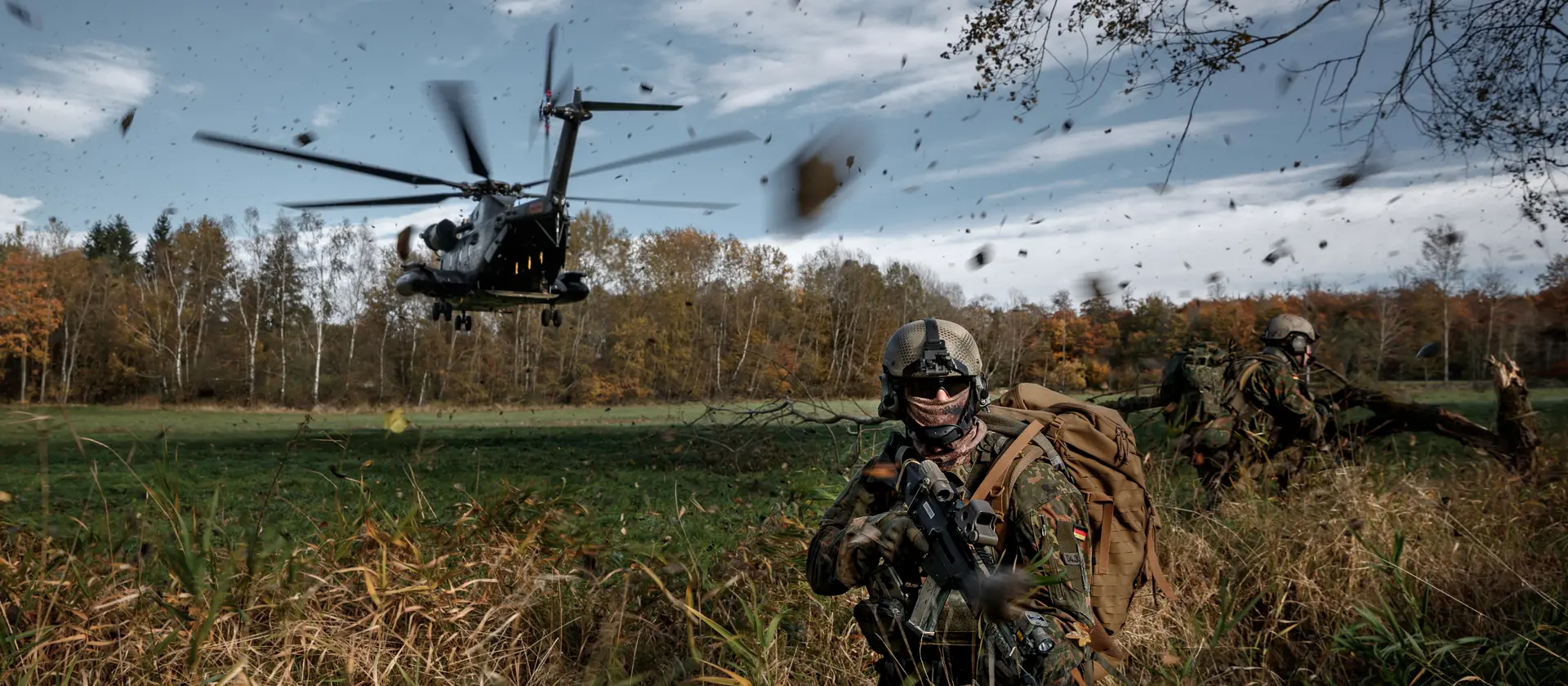 Ein Soldat im Feld. Im Hintergrund landet ein Hubschrauber