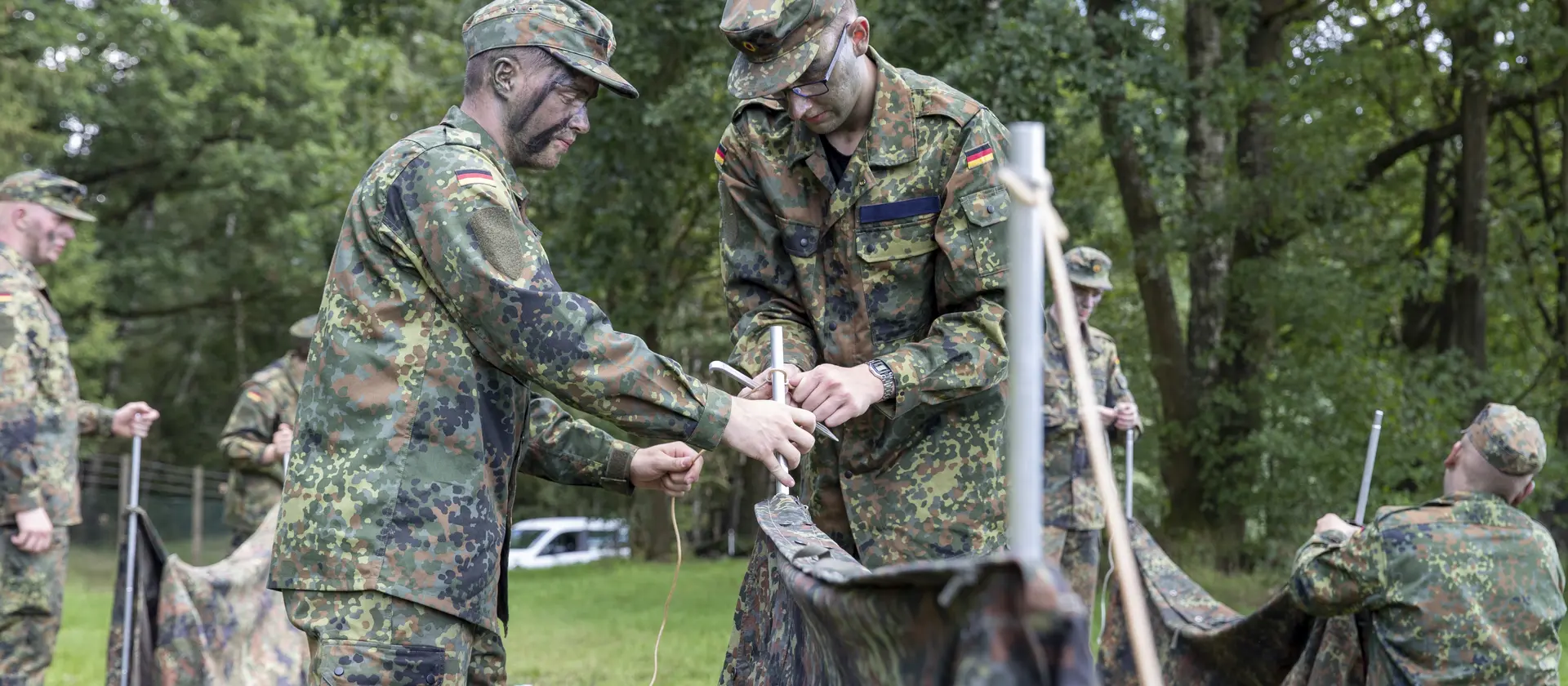 Soldaten in Tarnkleidung befestigen draußen im Gelände eine Plane
