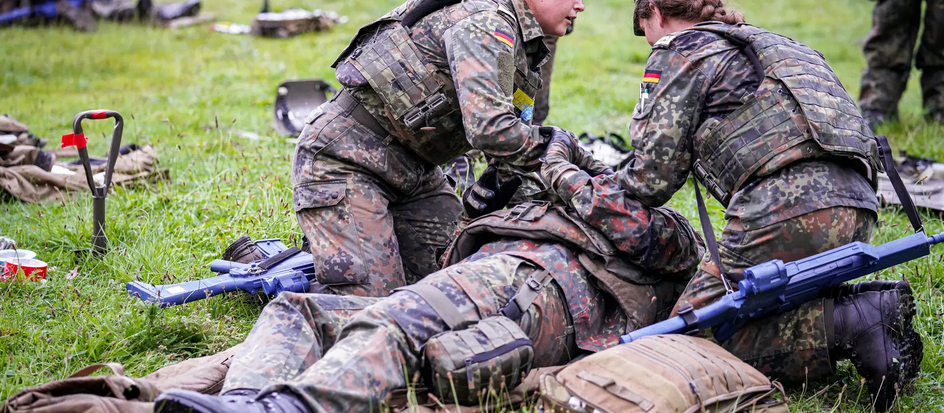 Zwei Soldatinnen versorgen einen verwundeten Kollegen, der auf der Wiese liegt.