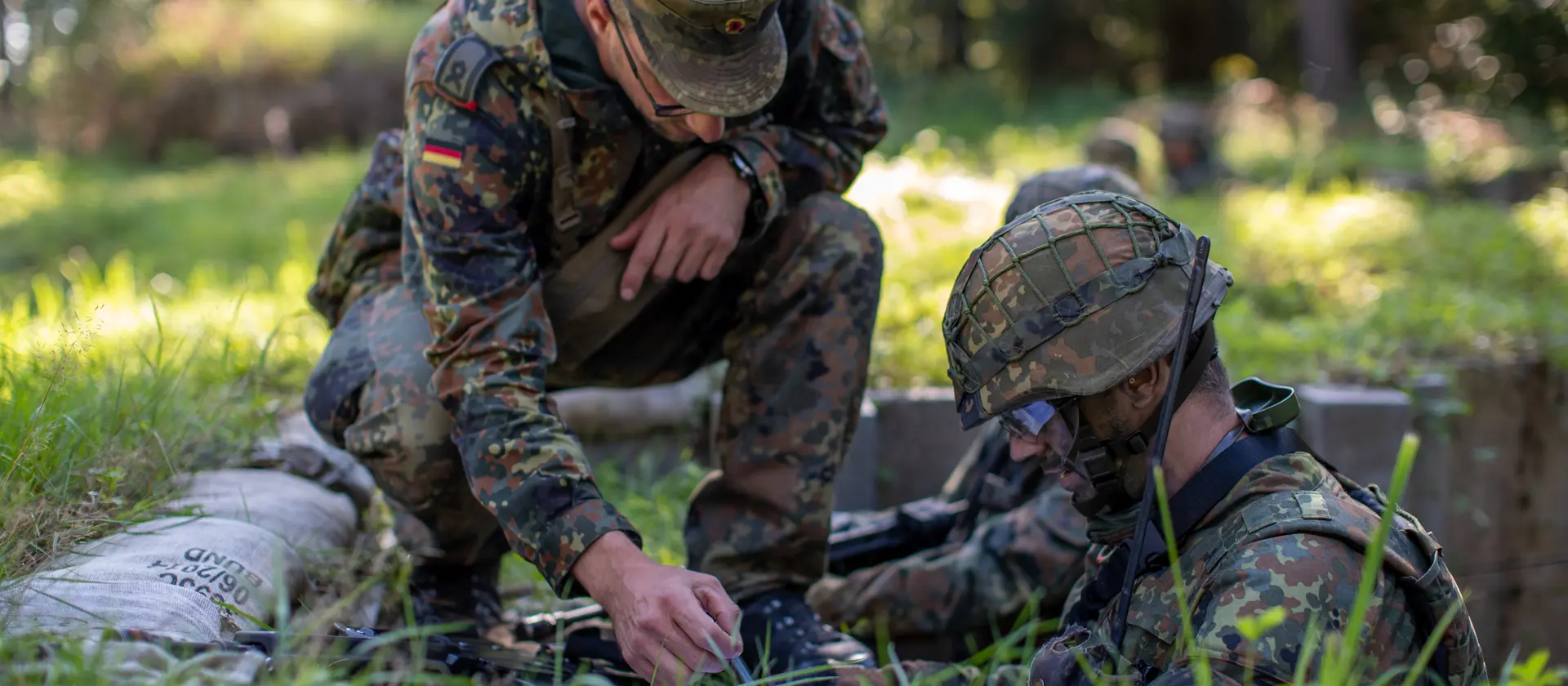 Zwei Soldaten in Tarnkleidung stehen auf einer Wiese im Gelände.