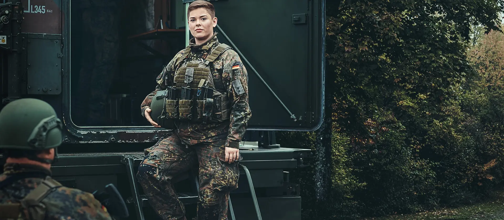 Ein Soldatin der Artillerietruppe steht auf den Stufen zu einem Transportfahrzeug und trägt ihren Helm unter dem Arm