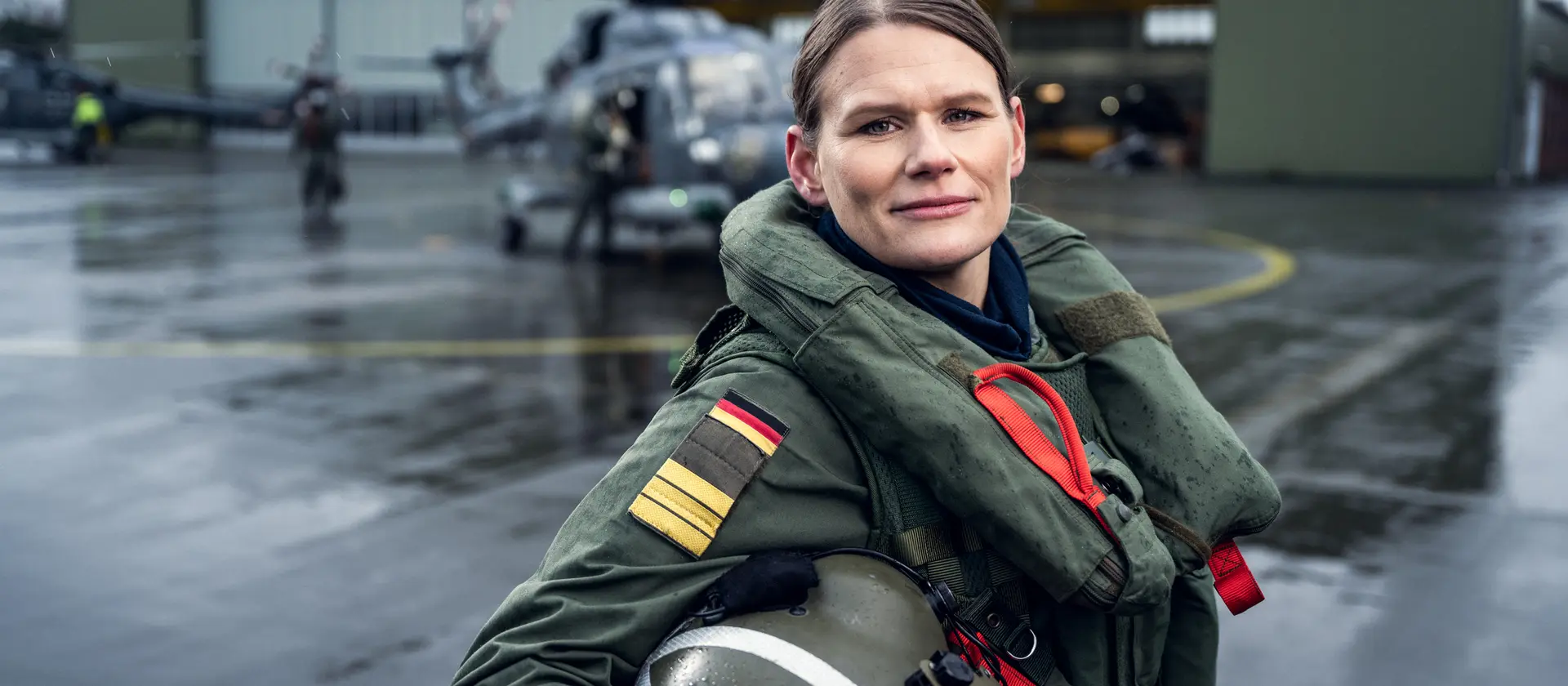 Eine Hubschrauberpilotin der Marine mit Helm in der Hand steht vor einem Hangar.