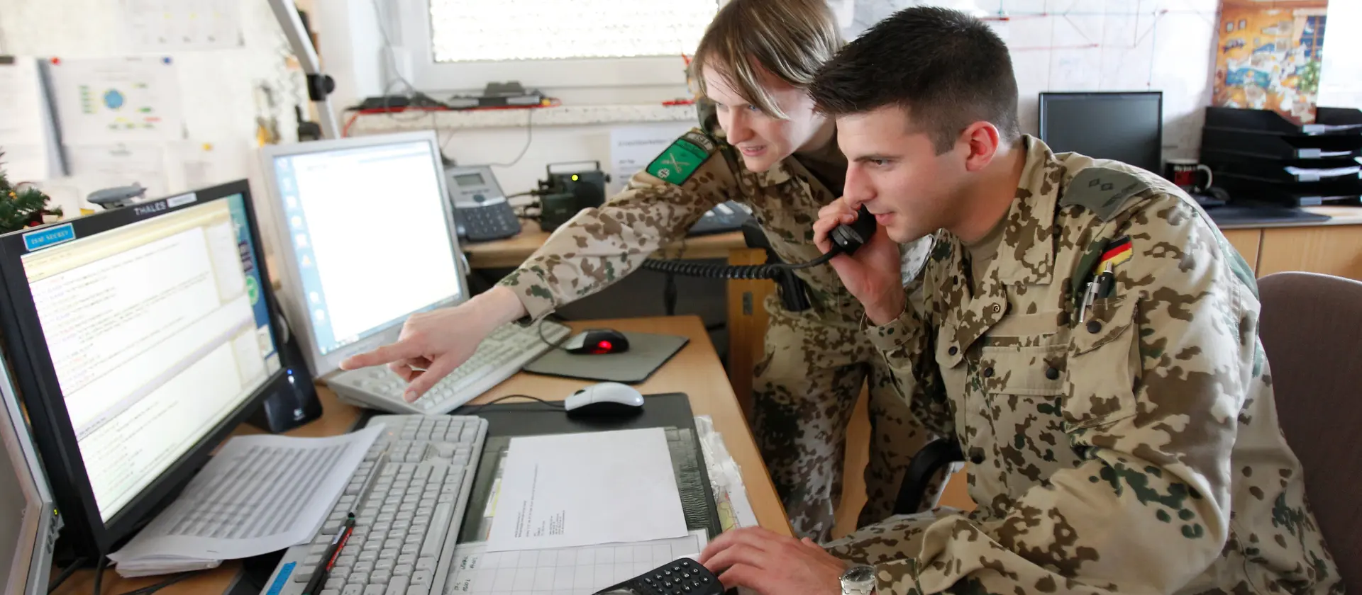 Ingenieure in Uniform besprechen sich am Schreibtisch vor zwei Monitoren