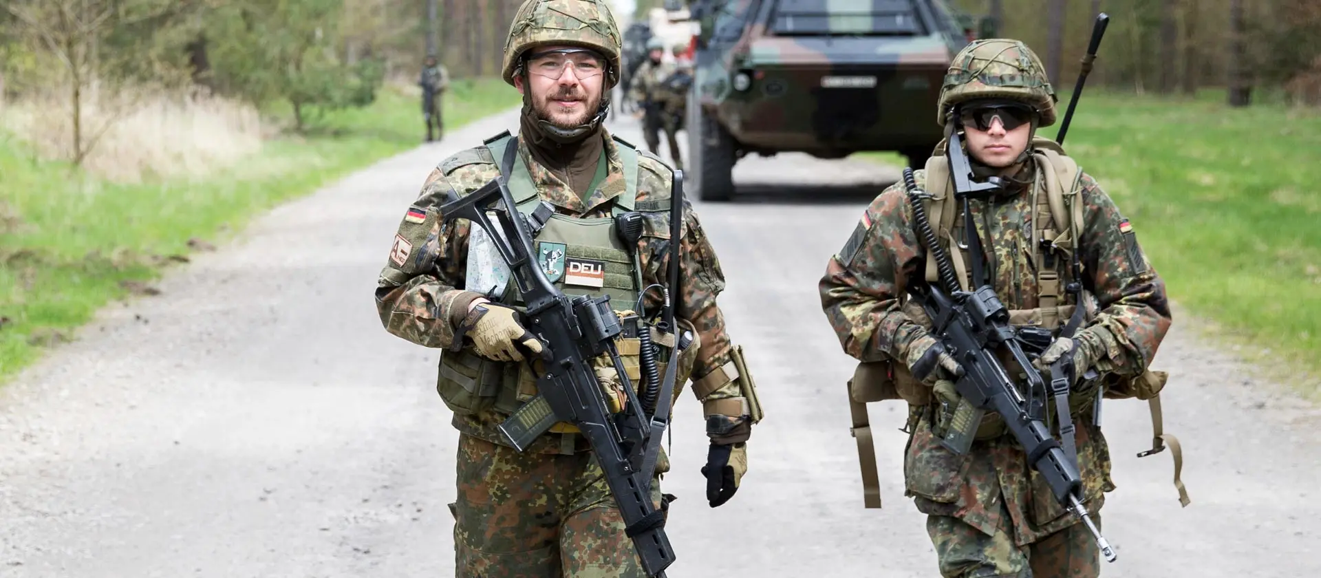 Soldaten der Jägertruppe patroullieren vor einem gepanzerten Fahrzeug