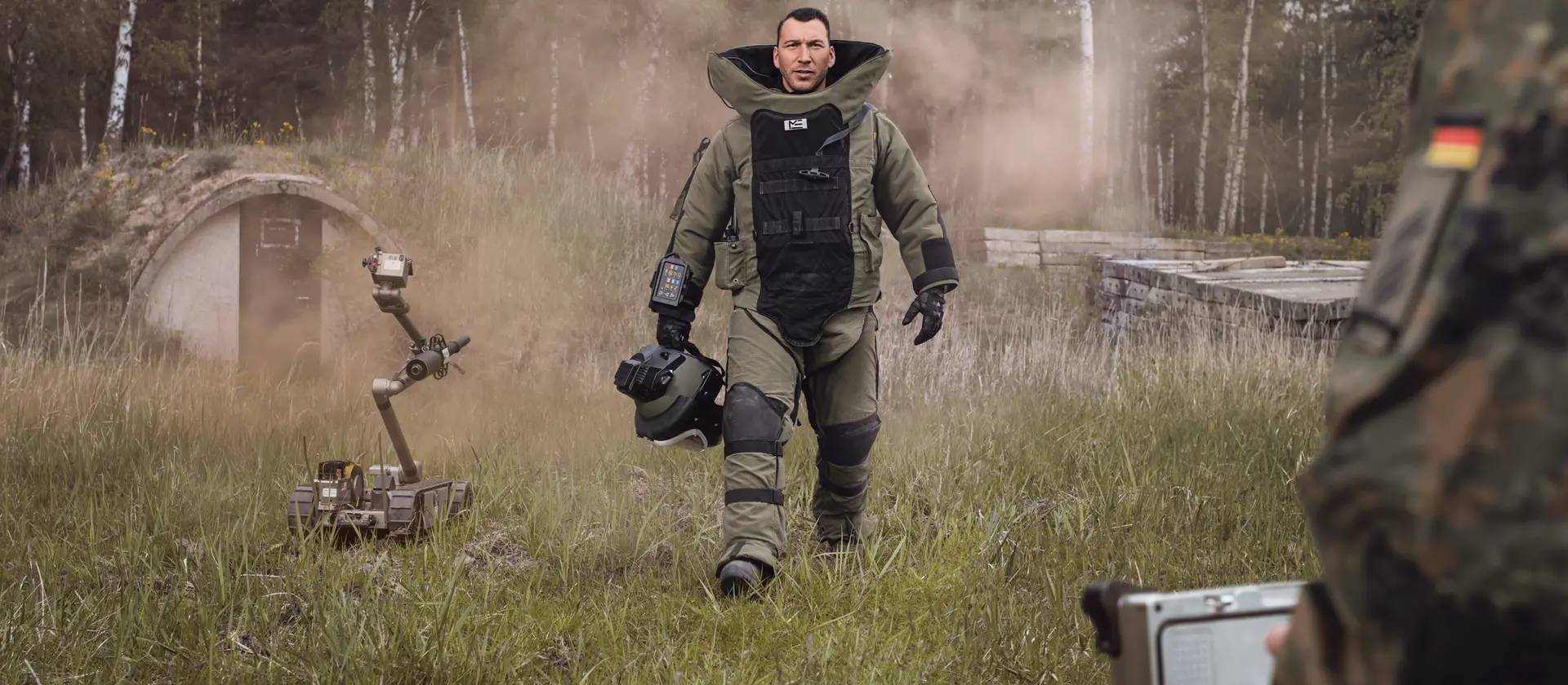 Ein Soldat der Kampfmittelabwehrtruppe im Schutzanzug läuft über eine Wiese und hält seinen Helm in der Hand