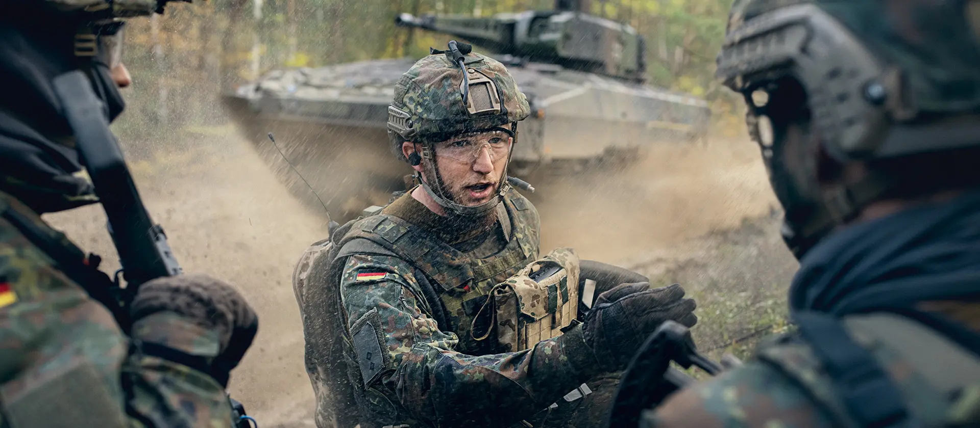 Ein Offizier der Panzertruppe steht im Gelände vor einem Panzer und weist seine Soldaten an