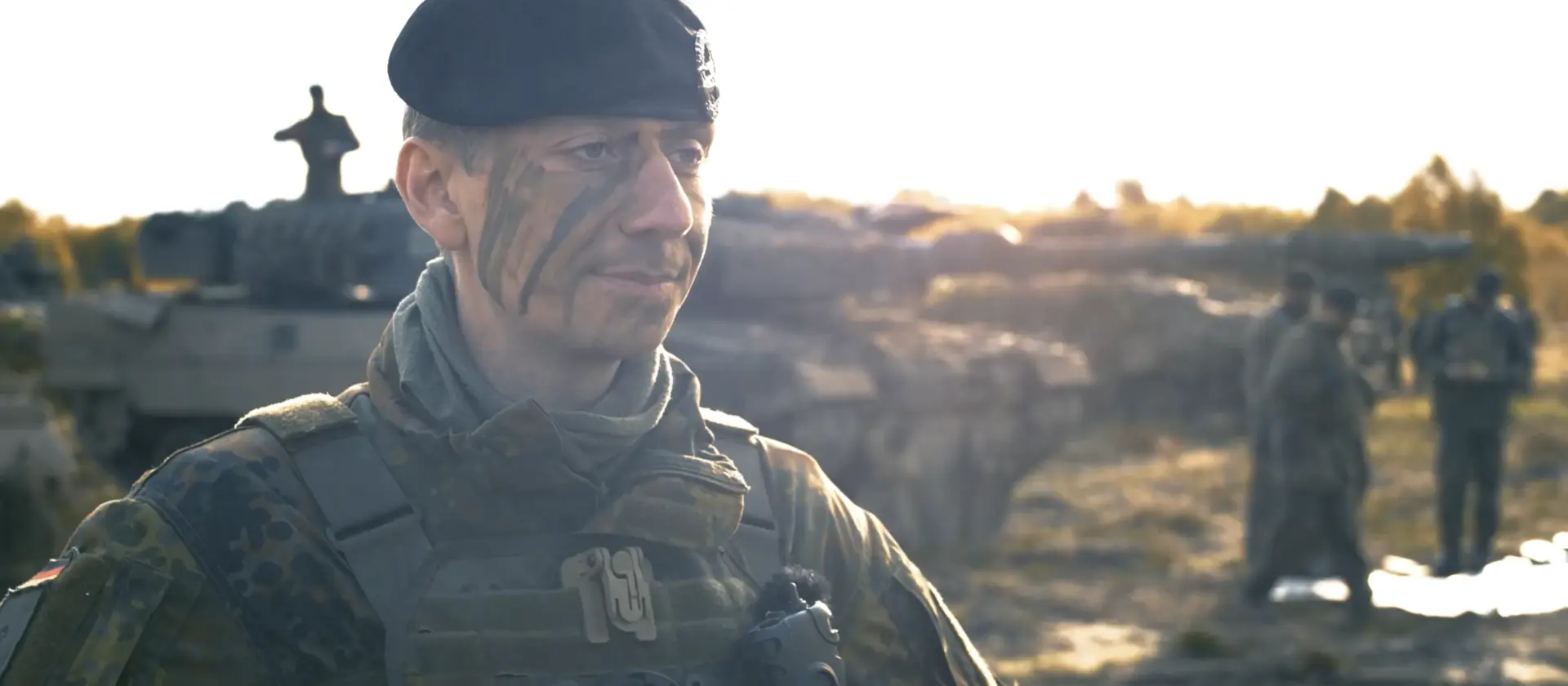 Soldat der Panzertruppe steht vor einem Panzer im Gelände
