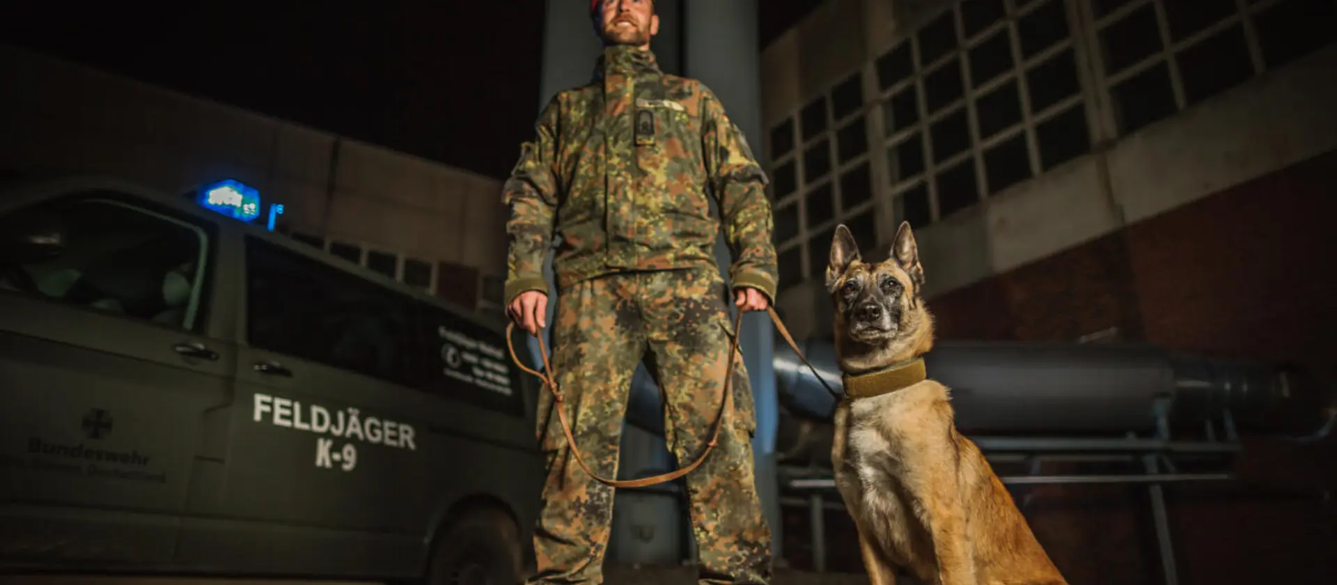 Ein Soldat der Feldjägertruppe steht mit seinem Diensthund vor einem Fahrzeug der Bundeswehr