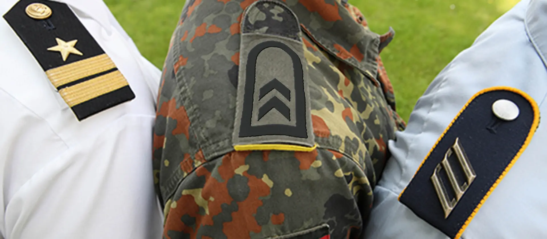 3 Schultern von Soldat_innen sind zu sehen. Die Abzeichen ihrer Dienstgrade sind im Bild zu sehen.