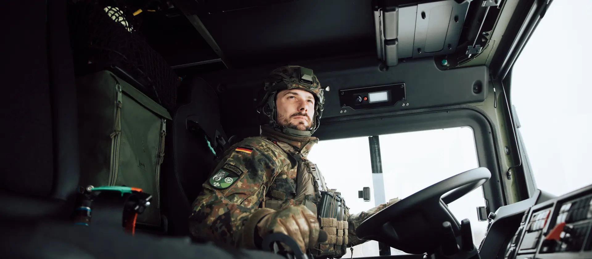 Ein Soldat in Flecktarnuniform und Helm sitzt auf dem Fahrersitz eines LKW