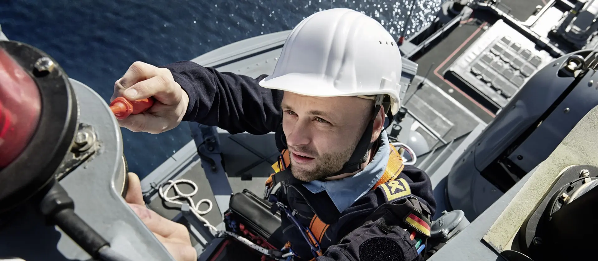 Soldat der Marinesystemelektronik ist auf einen Mast eines Schiffes geklettert und prüft eine Antenne.